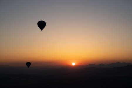landscape with hot air balloons black silhouette rising up to the sky at sunrise with beautiful high mountain panorama in the backgroundの写真素材
