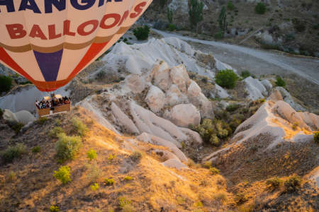 GOREME, TURKEY - AUGUST 3, 2021: Top view close up of colorful hot air balloon with basket full of tourists flying very close to the ground over the Cappadocia valley in the morning lightのeditorial素材