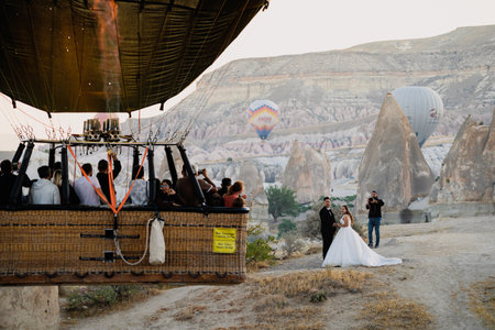 GOREME ,TURKEY - AUGUST 3, 2021: Close up of hot air balloon with basket full of tourist flying very close and spurring a wedding couple celebrating on the ground in Cappadociaのeditorial素材