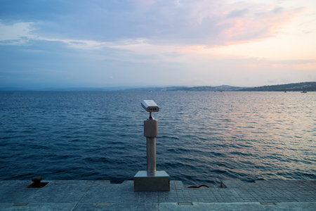 rear view closeup of coin operated metallic binoculars on concrete pier at the sea shore with sunset sky in the backgroundの写真素材