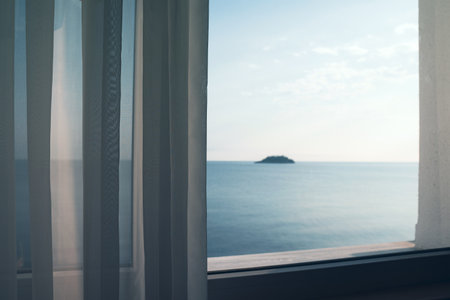 small ocean island seen through a window with transparent fabric curtainsの写真素材