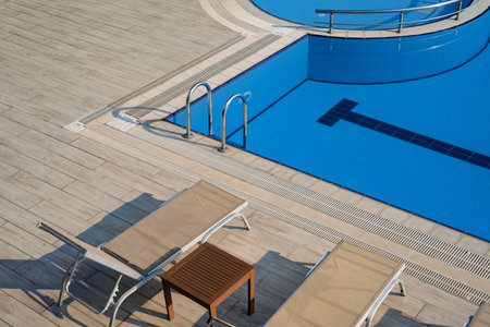 top view closeup detail of sunlounger chairs near a outdoor pool with blue water and chrome grab barsの写真素材
