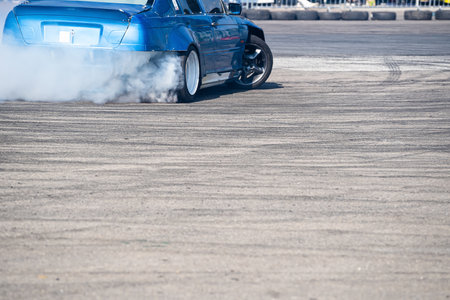 closeup rear view of blue sport car drifting on gray speed tarmac track with white smoke coming out...