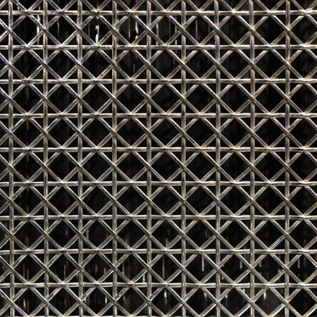 A closeup of a metal grid pattern featuring intricate crossed lines on a dark background for industrial designの写真素材