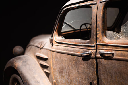 Aged vintage car captured from side view showcasing rust and broken glass window in a dim settingの写真素材