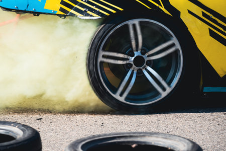 closeup side view of yellow sport car drifting on gray speed tarmac track with colored smoke coming out of the back tire wheel with copy space availableの写真素材