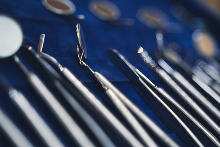 perspective view closeup of row of various basic steel chrome dental tools on display on blue background with shallow depth of fieldの写真素材
