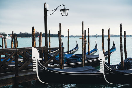 Classic gondolas floating near a rustic wooden dock in a Venetian canal with a calm water backdropの写真素材
