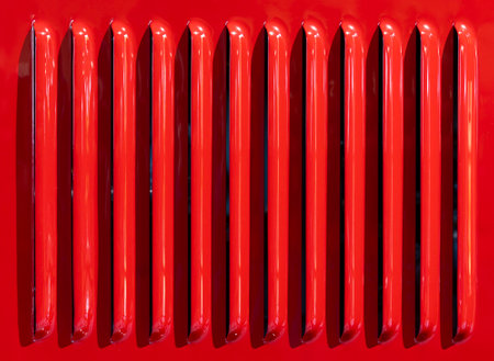 A closeup view of a red car grille featuring shiny vertical slats as part of a vintage automobile designの写真素材