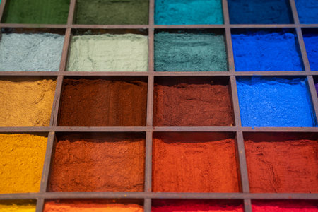 A vibrant arrangement of colorful pigments organized in a wooden grid with individual compartments