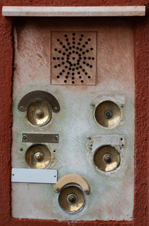 A vintage intercom panel featuring multiple bronze buttons set on a textured wall surface