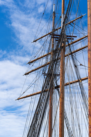 The intricate rigging of a tall wooden ship captured from below with a bright blue sky in the backgroundの写真素材