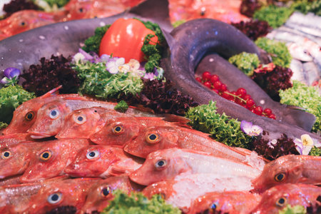 Fresh red fish and eel displayed on ice with decorative greens and vegetables in a seafood market