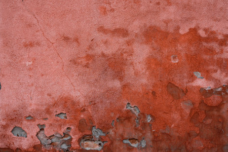 An aged red stucco wall featuring weathered textures and peeling paintの写真素材