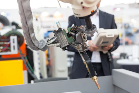 Industrial welding robotic arm, blurred operator in the background