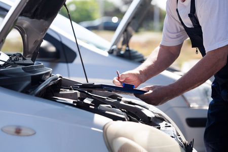 Auto mechanic checking car engine and writing on the clipboardの写真素材