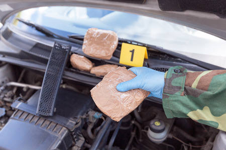 Policeman holding drug package found in engine compartment of a carの写真素材
