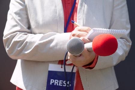 Female journalist at press conference, writing notes, holding microphoneの写真素材