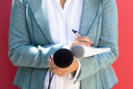 Female journalist at news conference, writing notes, holding microphone