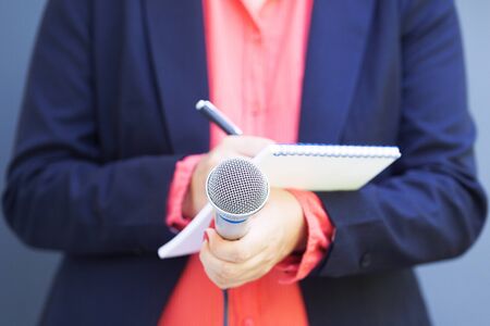 Female journalist at press conference, writing notes, holding microphoneの写真素材