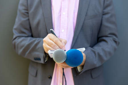 Journalist at news conference or media event, writing notes, holding microphoneの写真素材