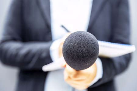 Journalist holding microphone at news conference or media event and writing notes