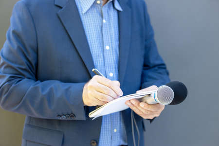 Journalist at media event or press conference, holding microphone, writing notes. Broadcast...
