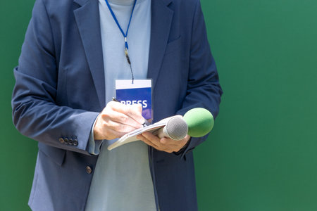 News reporter at press conference or media event, holding microphone, writing notes. Broadcast...