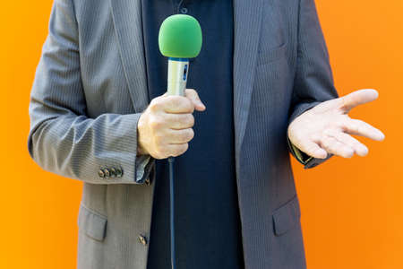 Reporter reporting from media event, holding microphone, making a hand gestureの写真素材