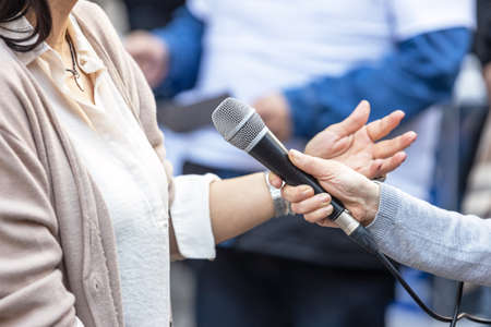 Journalist holding microphone making media interview with female politician or business womanの写真素材