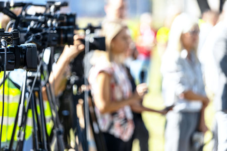 Covering an media event with a video camera, unrecognizable blurred female reporter holding microphone in the background.の写真素材