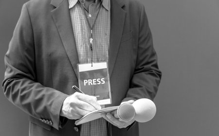 Male journalist at news conference or media event, holding microphone, writing notes. Journalism concept.の写真素材