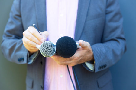 Reporter or journalist at media event, holding microphone, writing notes. Broadcast journalism concept.の写真素材