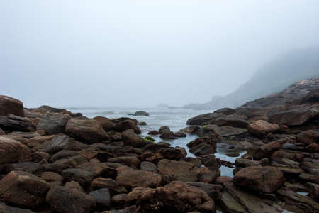 Foggy beach with rocks and mist at nightfallの写真素材