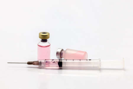Isolated glass and plastic vaccine bottle one lying down with colored liquid and a full of colored liquid syringeの写真素材