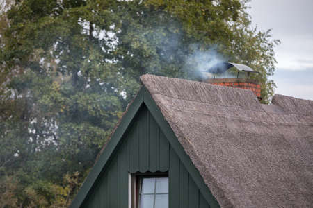 smoking chimney on top of thatched roofの写真素材