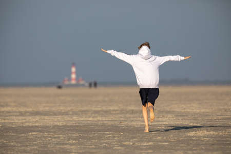 Teenager runs with outstretched arms across the wide sandy beachの写真素材