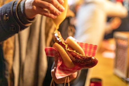 applying mustard on a sausage in a bread rollの写真素材