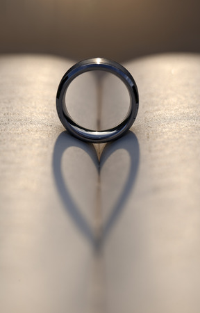 Wedding ring between the pages of an old book with the sunlight casting a heart shaped shadow の写真素材
