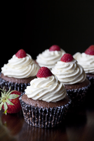 Chocolate cupcakes with vanilla icing topped with strawberriesの写真素材