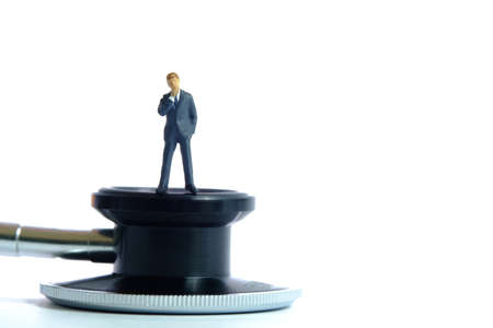 Health conceptual miniature people photography â businessman stands above stethoscope. Image Photoの写真素材