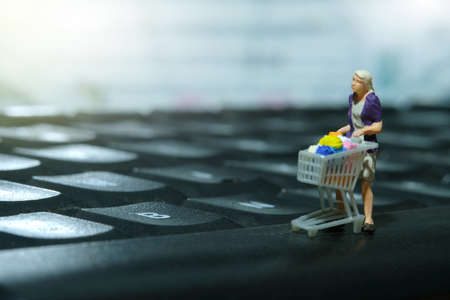 A woman doing online shopping. Walking with cart shop above keyboard. Miniature people figurines toys conceptual photography.の写真素材