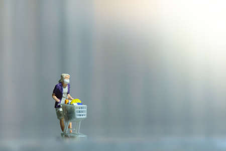 A woman doing safe solo shopping at supermarket wearing a face mask. Miniature people figurines toys conceptual photography.の写真素材