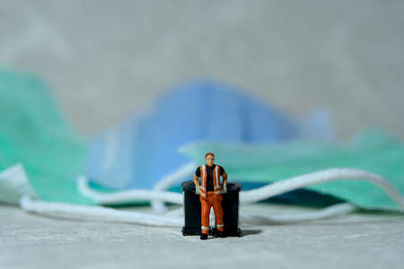 Cleaning workers carry disposable mask rubbish that has been used in the trash bin. Medical waste conceptual photo. Miniature people photography.の写真素材