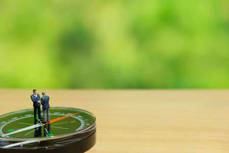 Business strategy conceptual photo - Two miniature businessman make handshake partnership agreement above compassの写真素材