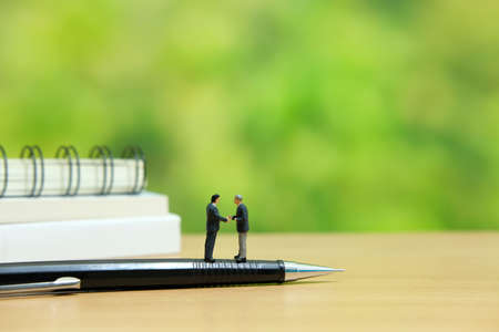Business strategy conceptual photo - Two miniature businessman make handshake partnership agreement standing above penの写真素材