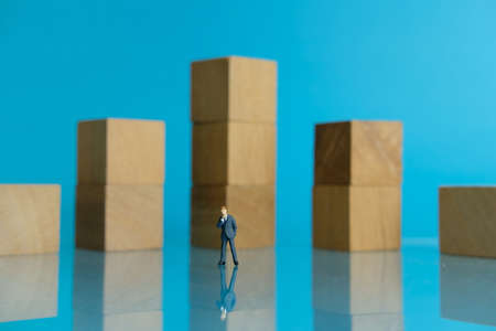 Miniature business concept - thinking young businessman standing in front of wooden chartの写真素材