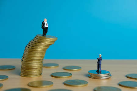 Miniature business concept - business man standing above golden coin stackの写真素材