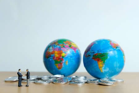 Miniature people business concept -Global trade partnership, with businessman, coin stack and globeの写真素材