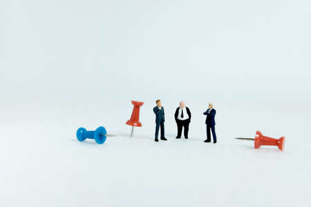 Miniature business concept - group of businessman standing beside red and blue thumbtack push pin with white backgroundの写真素材